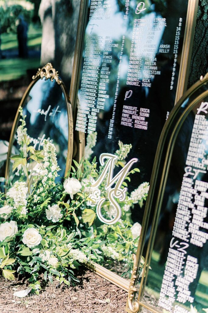 Elegant seating charts with gold frames and floral arrangements displayed outdoors.