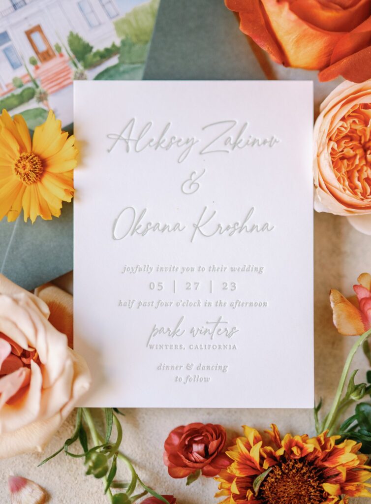 Wedding invitation with flowers. Text includes names Alexey Zakinov and Oksana Krishna, date 05.27.23, and venue Park Winters, California. Dinner and dancing mentioned.