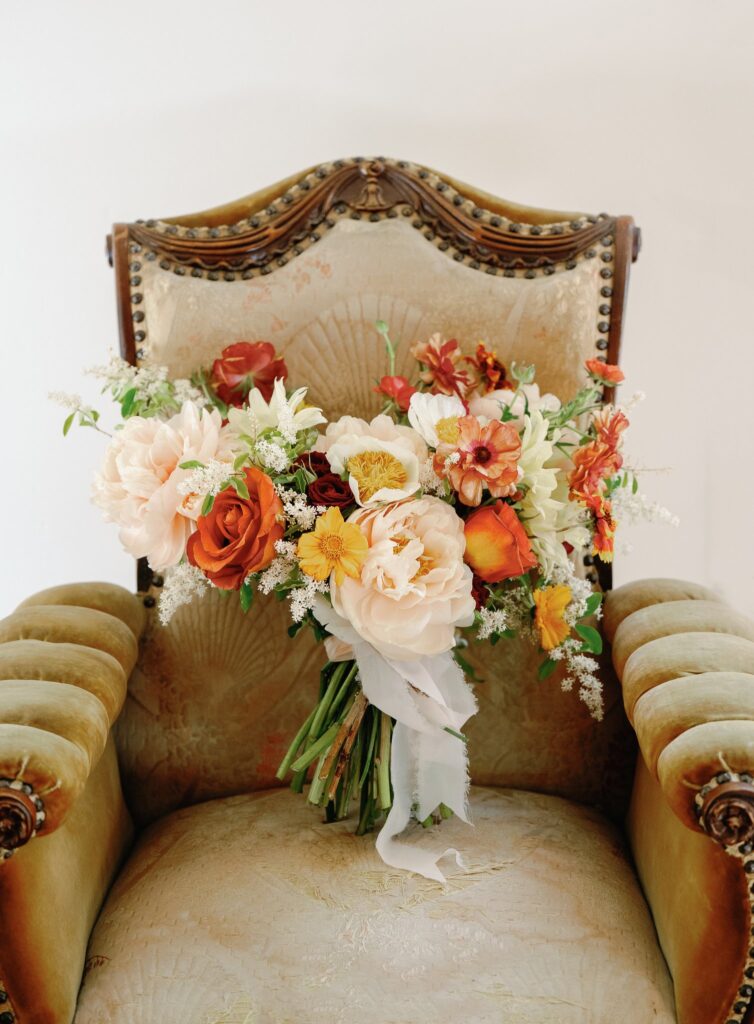 A bouquet of colorful flowers, including roses and daisies, is placed on an ornate vintage chair with a velvet cushion.
