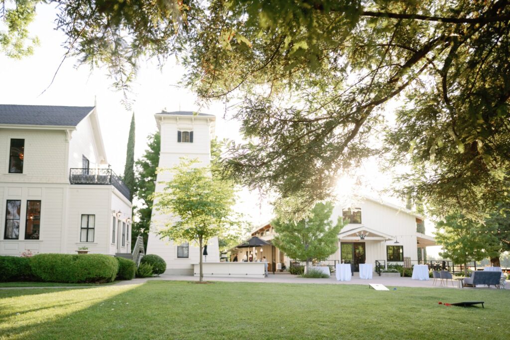 A scenic view of a park-like setting with a grassy lawn, trees, and two light-colored buildings under a bright sky.