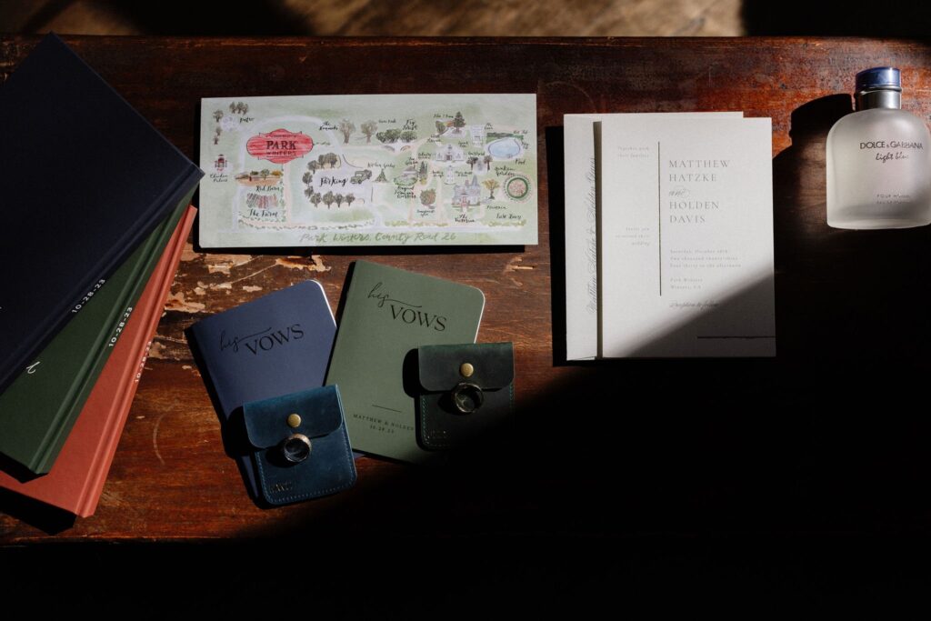 A wooden table with wedding vows booklets, a park map, invitation cards, and a bottle of Dolce & Gabbana perfume.