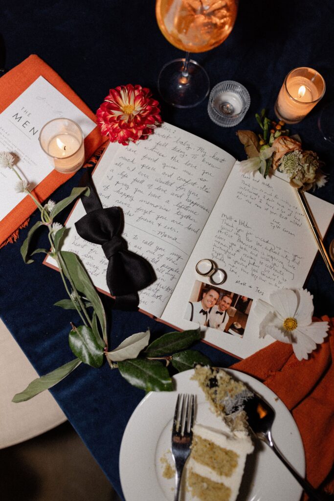 Handwritten letters, a bow tie, flowers, candles, and wedding rings on a table with cake and drinks.