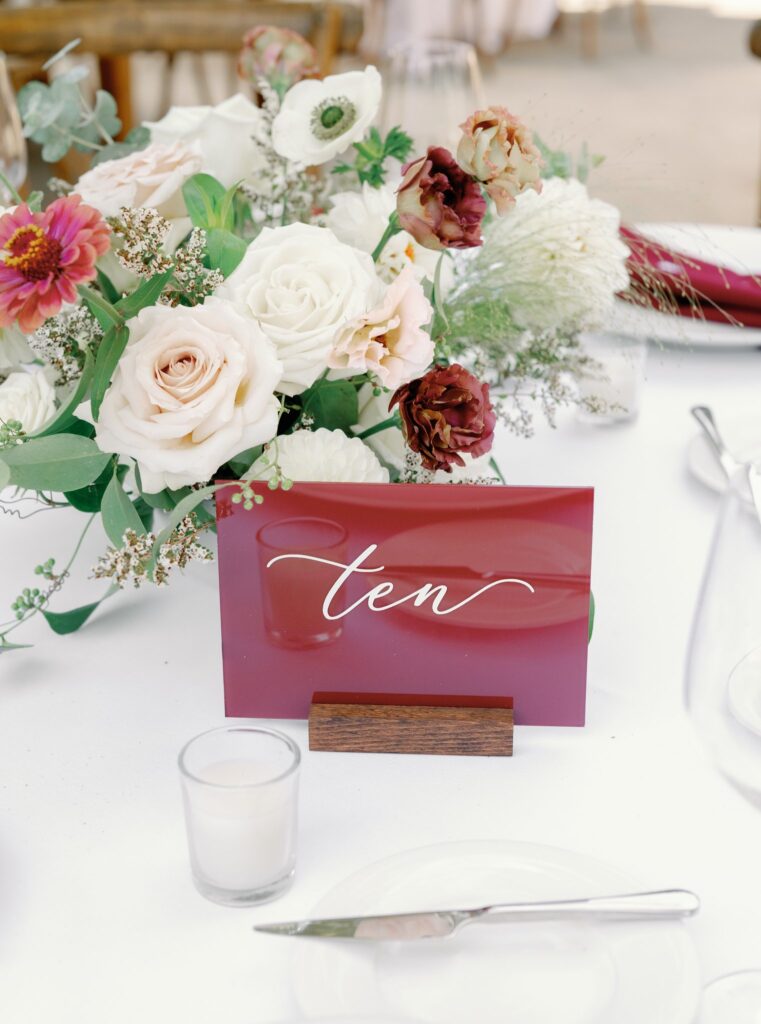 A table centerpiece featuring a floral arrangement with roses and a red card displaying the word "ten" in cursive.