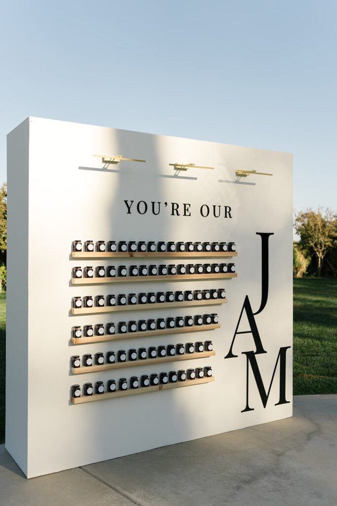 Display board with small jars arranged neatly, featuring the text "You're Our Jam" and a large letter "JAM" on the right side, set outdoors in sunny weather.