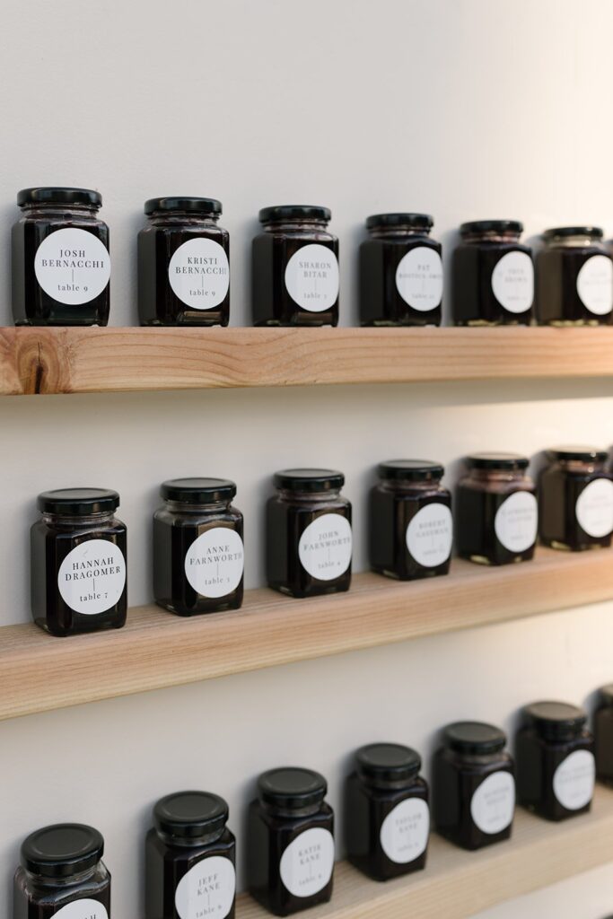 Jars with name labels on wooden shelves, arranged in rows against a plain wall.