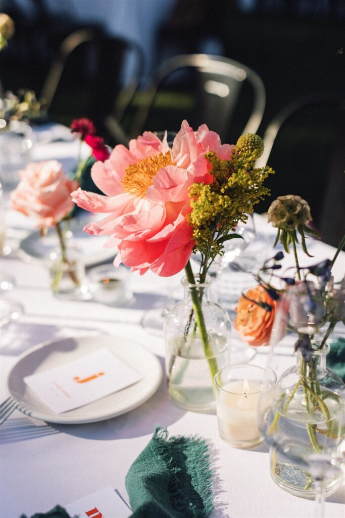 A table set for a Napa Valley wedding features a white tablecloth, elegant place settings, and glass vases filled with bright pink and yellow flowers.