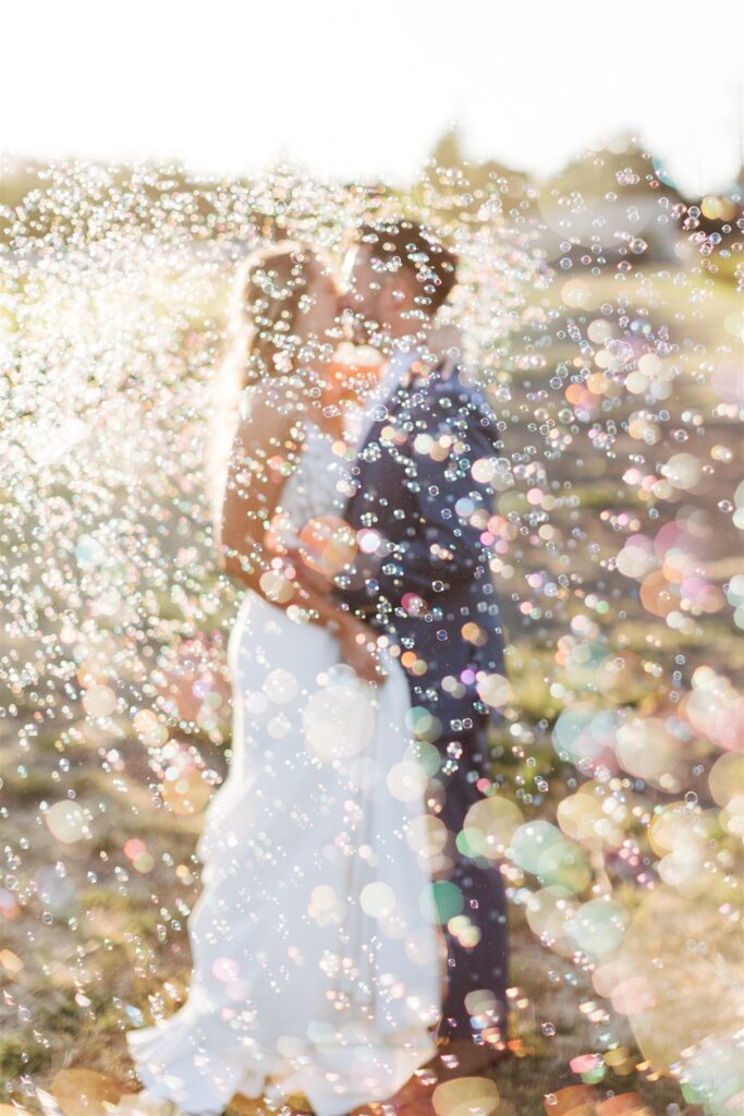 A couple stands close together in the dreamy outdoors of a Napa Valley wedding, surrounded by a shower of bubbles.