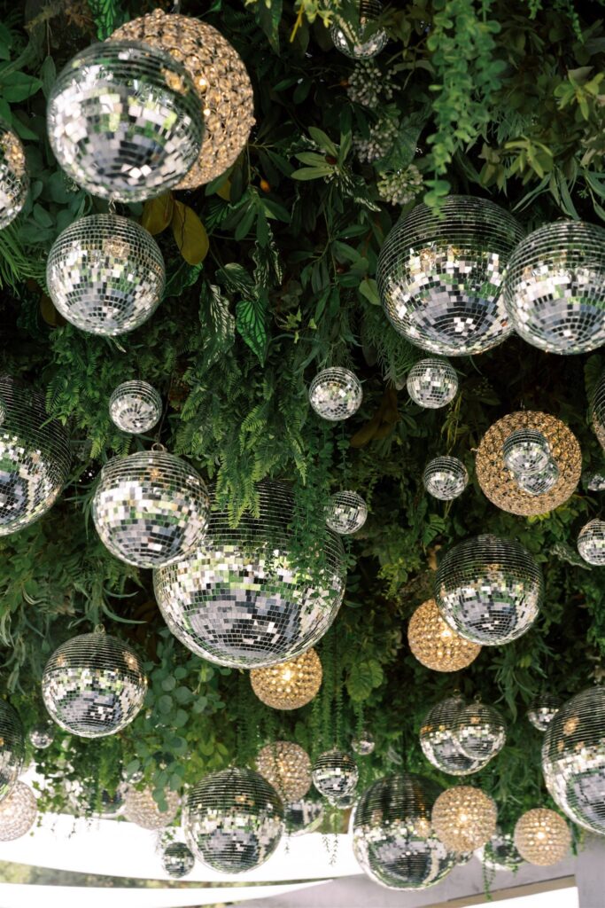 A ceiling decorated with mirrors, greenery, and round, silver reflective disco balls mixed with clusters of small golden lights.