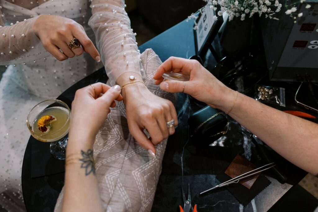 Person assisting another with a bracelet at a table, with a cocktail and tools nearby.