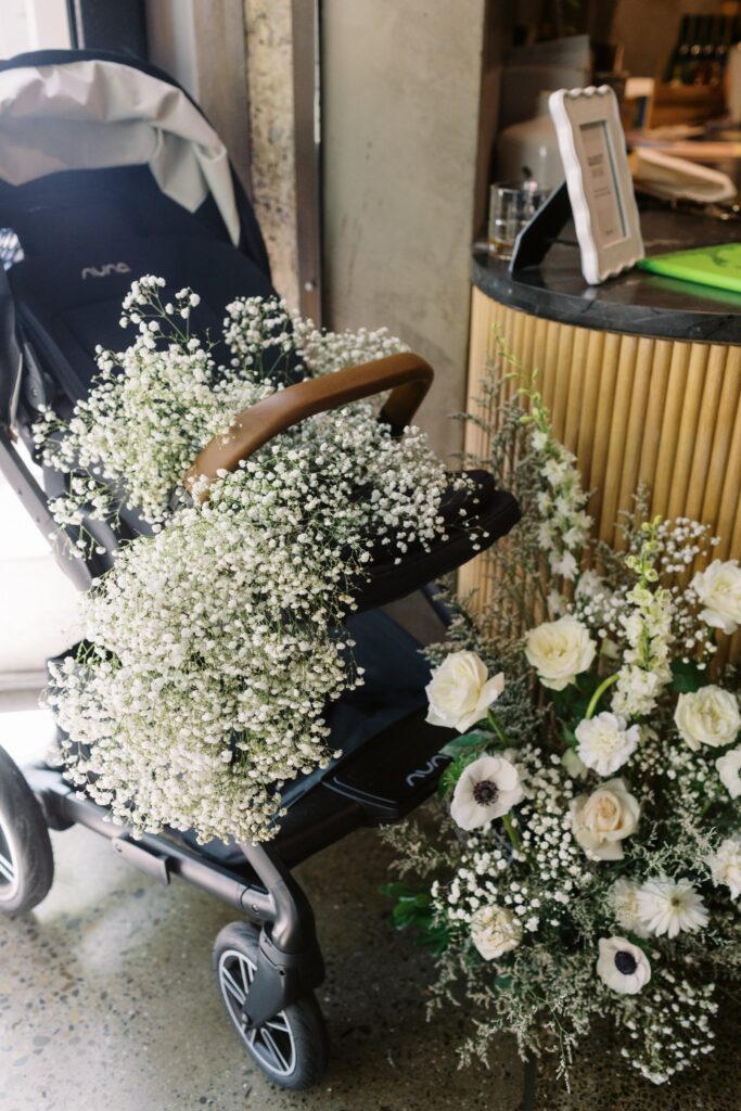 A stroller filled with white baby's breath and surrounded by various white flowers, positioned near a counter.