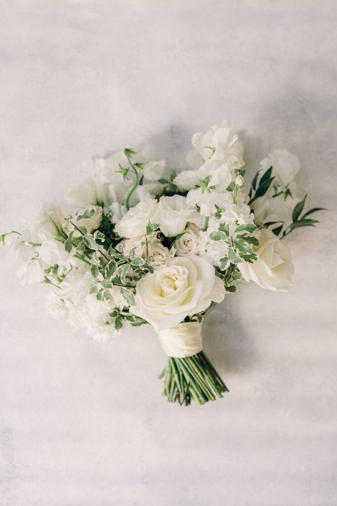 A bouquet of white roses and greenery against a light background.