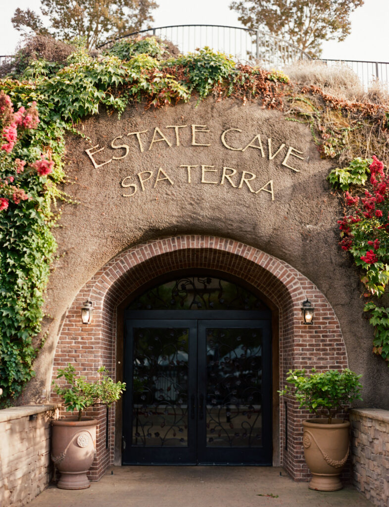 Entrance to Estate Cave Spa Terra, featuring a stone archway with greenery and potted plants on either side.