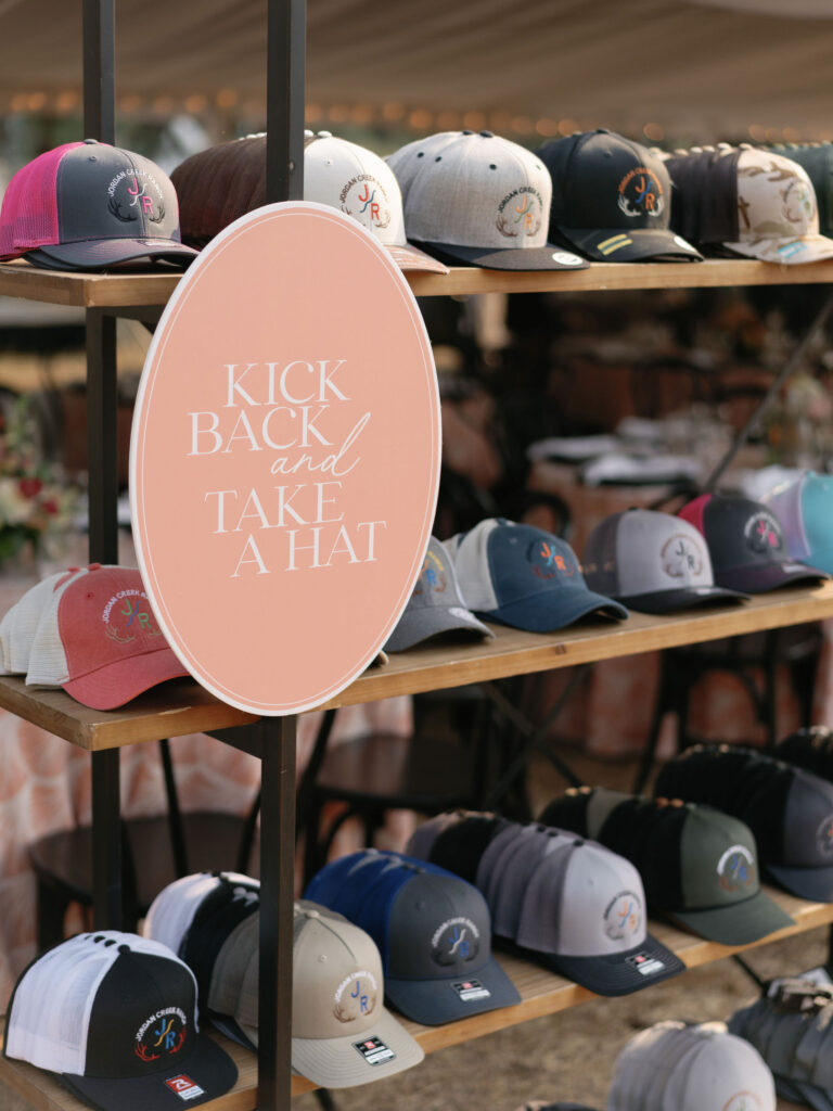 Display of various baseball caps on shelves with a round sign that reads, "Kick Back and Take a Hat.