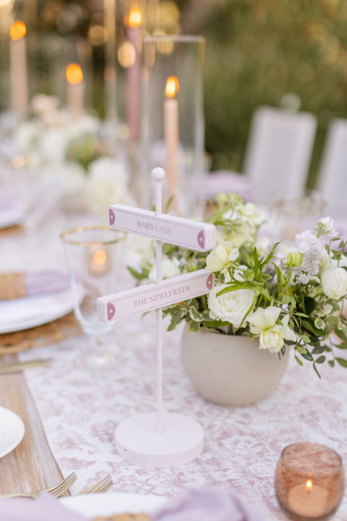 Elegant table setting with a lace tablecloth, lit candles, floral centerpiece, and a small sign reading "Maris Lane The Newlyweds.