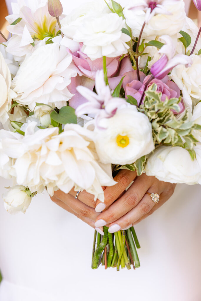 A person holding a bouquet of white and light purple flowers, their manicured hands and rings visible on their fingers—perfect inspiration for an Estate Yountville Wedding Planner seeking elegant floral details.