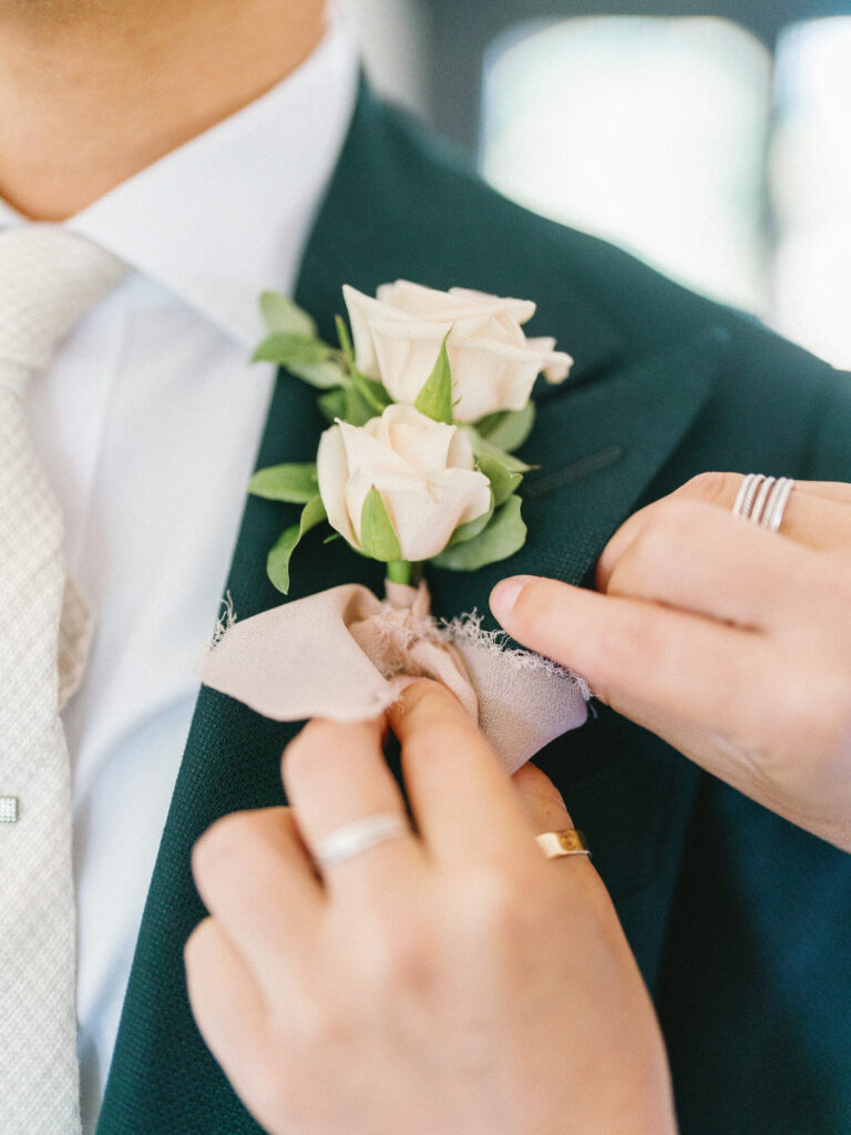 A person adjusts a boutonniere with pale roses on a suit jacket.