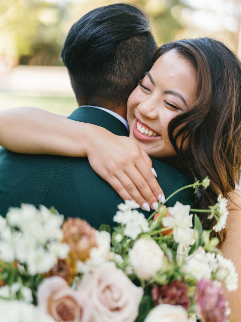 A smiling woman embraces a man outdoors, holding a bouquet of assorted flowers.