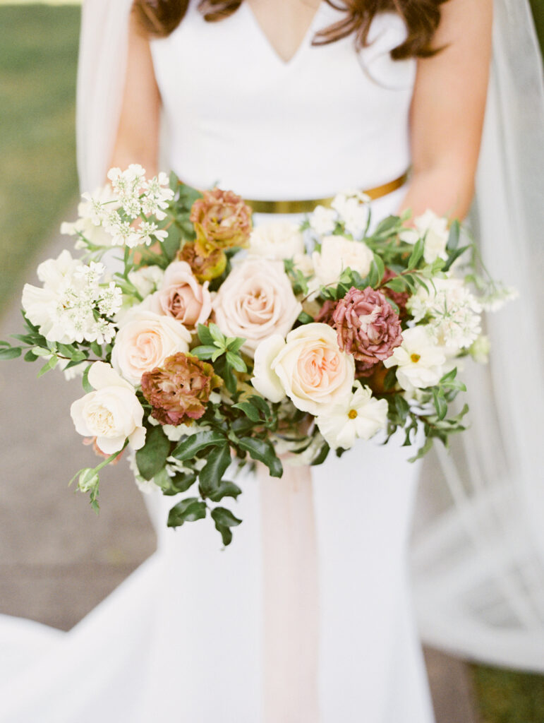 A bride in a white dress holds a bouquet with pink, white, and beige flowers.