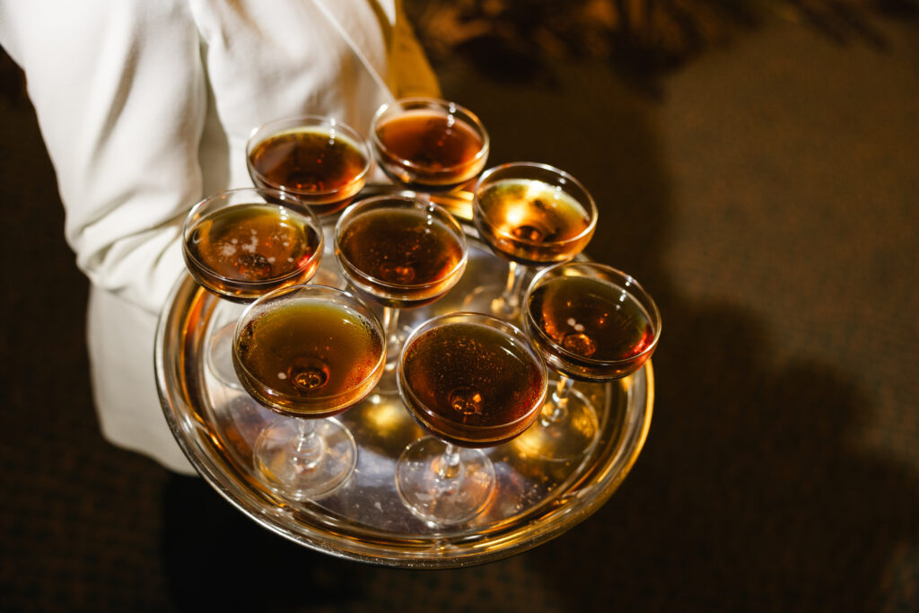 A server holding a silver tray with eight filled champagne coupes.