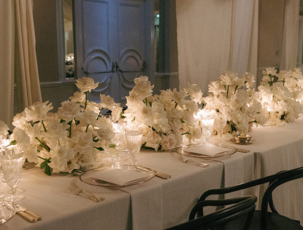 Elegant table setting with white floral centerpiece, crystal glassware, and lit candles on a long dining table.