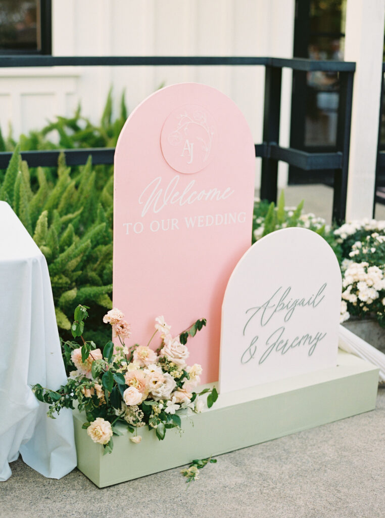 Wedding welcome signs reading "Welcome to Our Wedding" and "Abigail & Jeremy" with flower decorations, displayed outdoors.