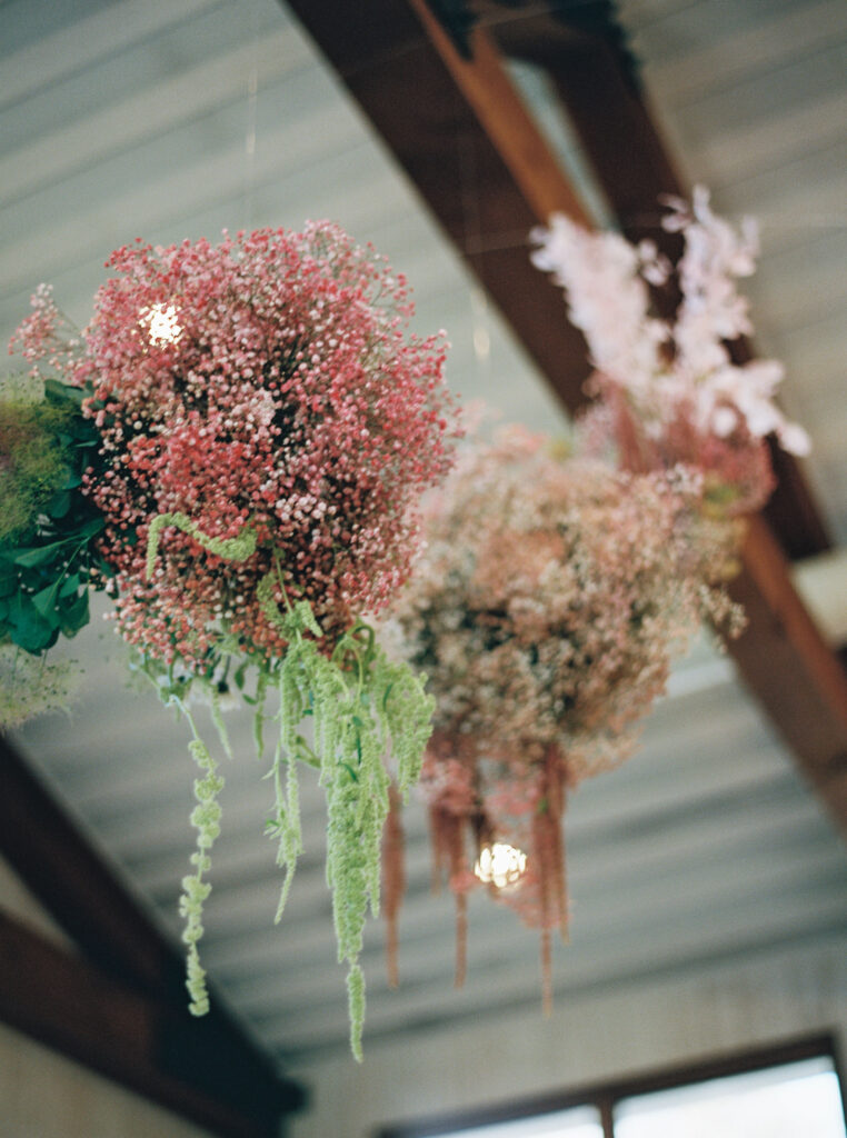 Hanging floral arrangements with pink and green flowers suspended from a wooden ceiling.