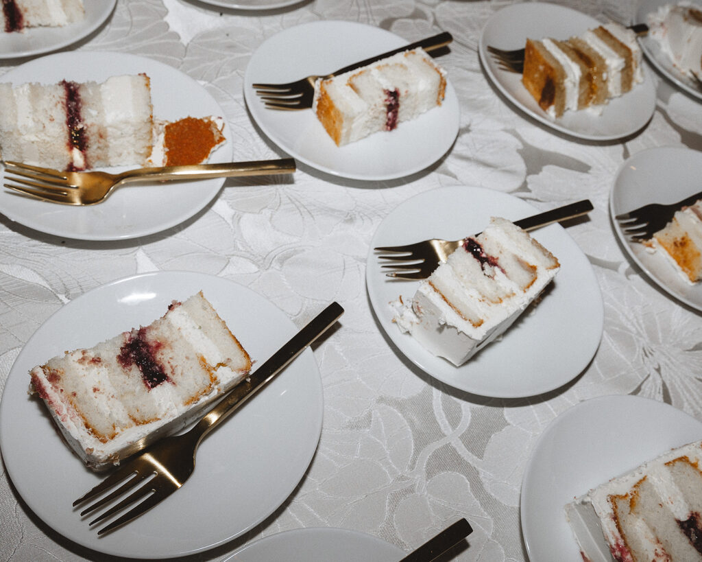 Slices of layered cake with white frosting and filling on plates with forks, arranged on a table with a white tablecloth.