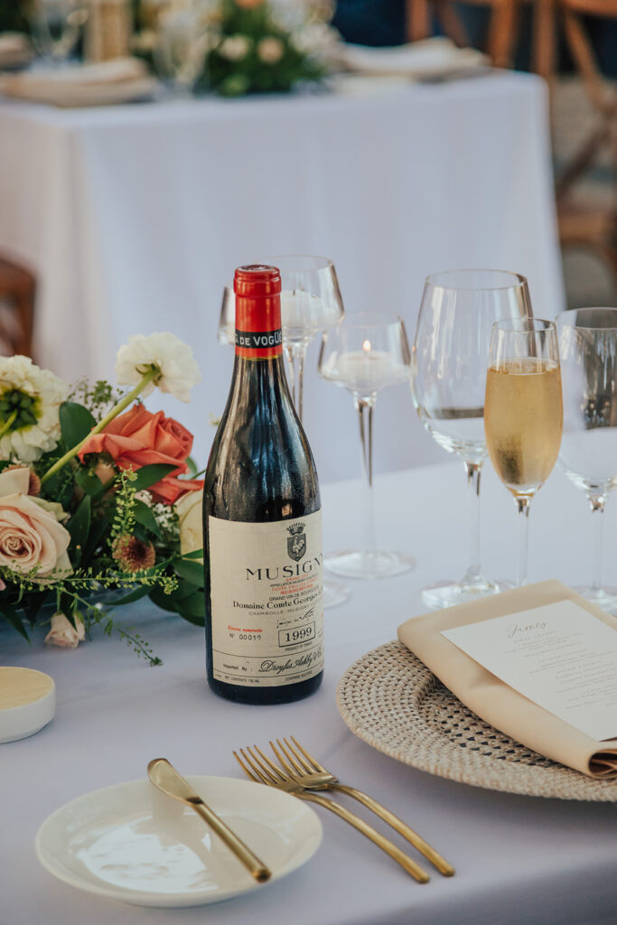 A bottle of wine is on a table set with flowers, wine glasses, a champagne flute, and a menu.