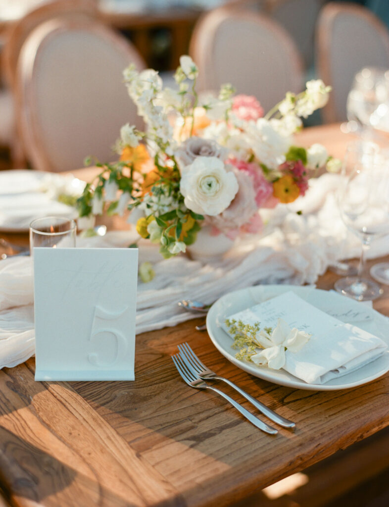 Table setting with a floral centerpiece, a plate with a napkin and small flowers, and a table number card.