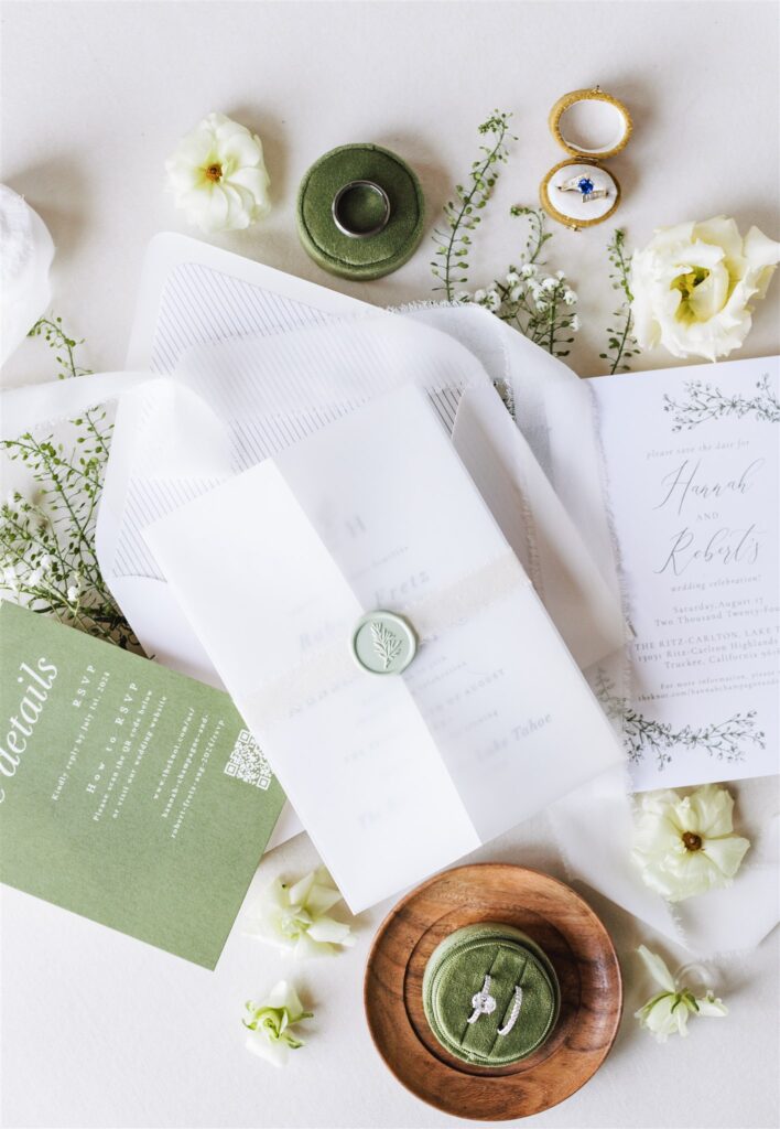 Elegant wedding invitation set with green wax seal, floral elements, and rings displayed on a white surface.