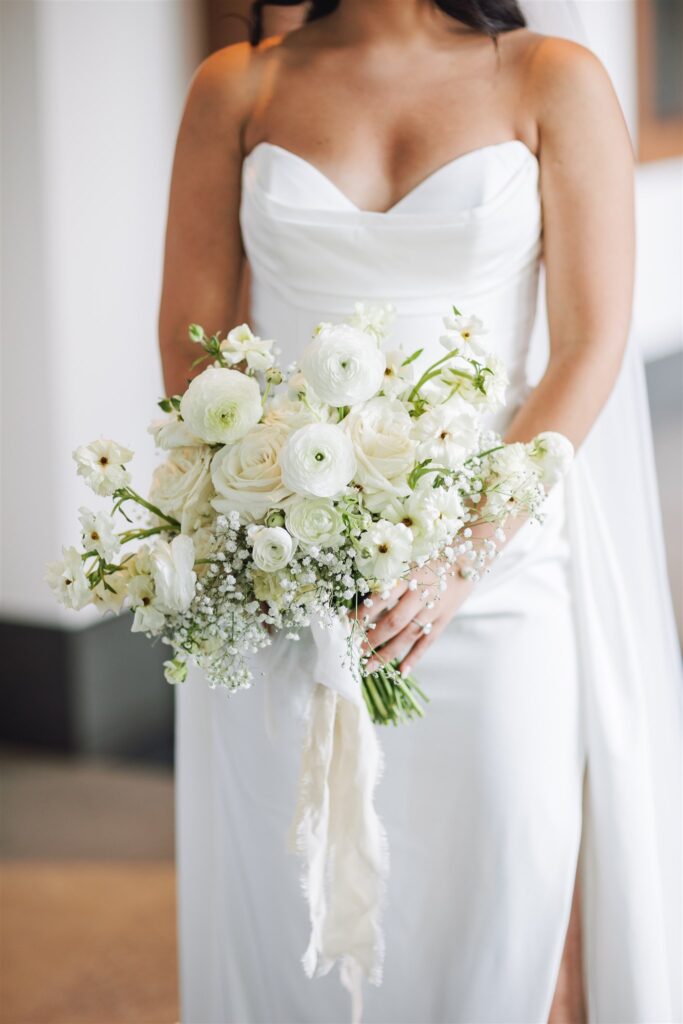 Bride in a white dress holding a bouquet of white flowers with hints of greenery.