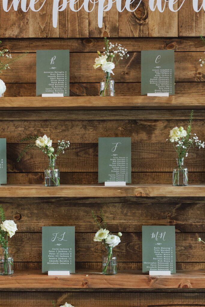 Wooden shelves displaying floral arrangements and seating cards with letters and names.
