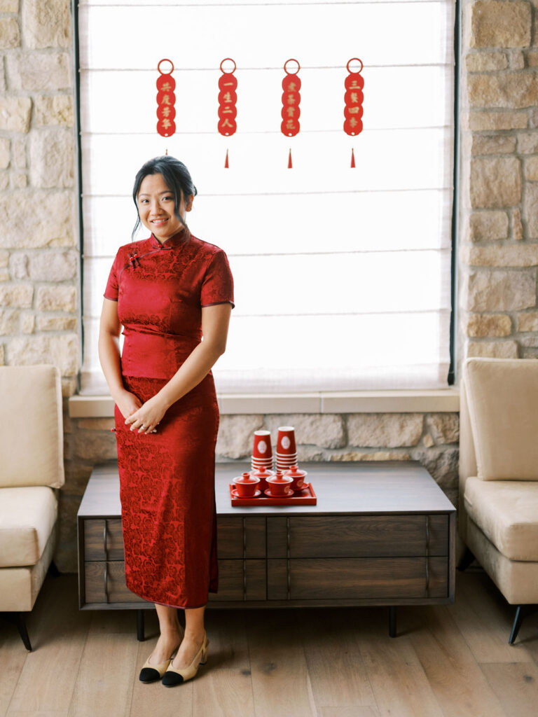 A woman in a red dress stands in a room with stone walls and Chinese decorations in the background.