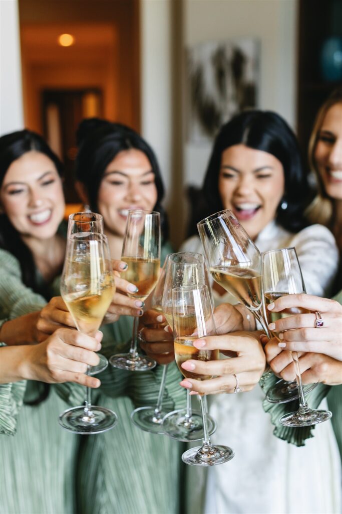 Five people clink champagne glasses in a celebratory toast, smiling and standing close together indoors.