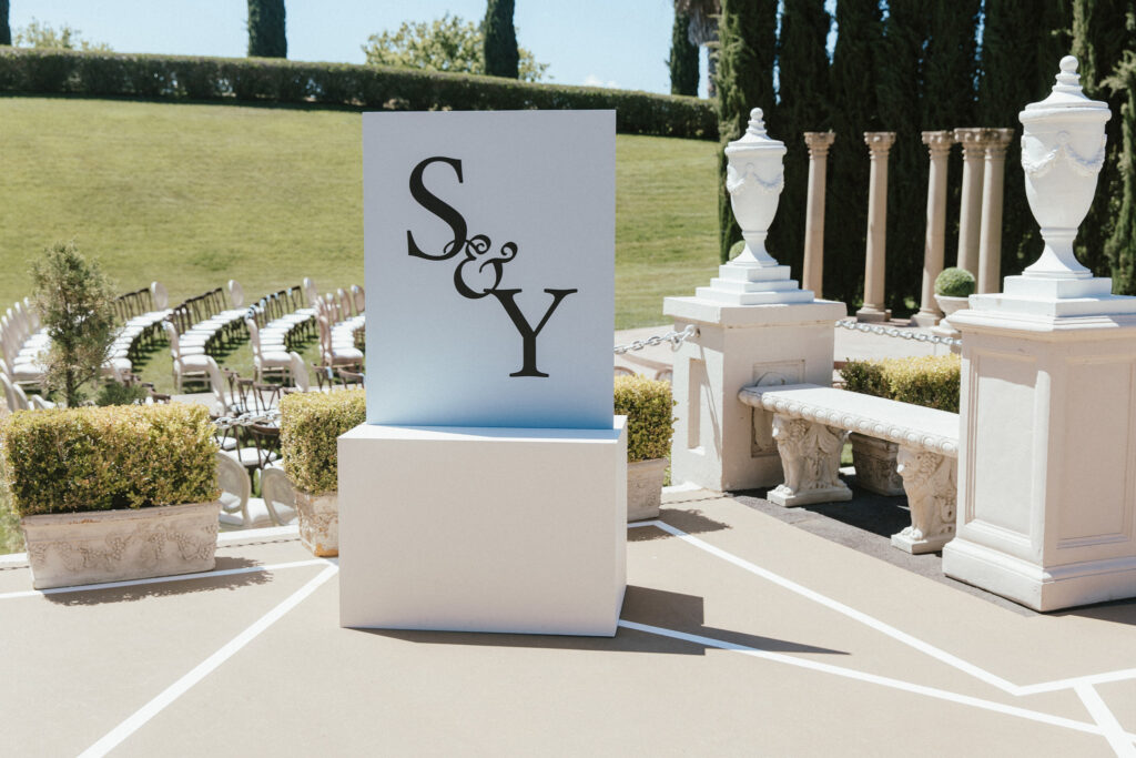 Outdoor setup with chairs and greenery for an event. A large display with "S & Y" is in the foreground.