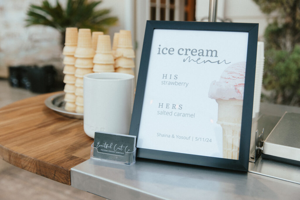 A table displays a framed ice cream menu listing flavors, stacked cones, a mug, and a business card holder.
