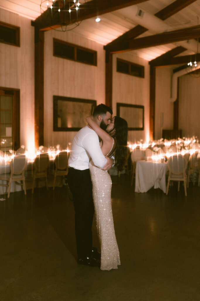 A couple embraces and kisses on a dimly lit dance floor in an elegant room with wooden walls and ambient lighting.