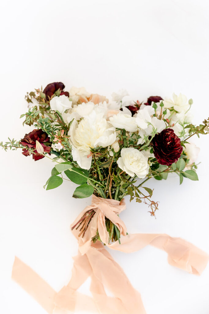 Bouquet of white and dark red flowers with green foliage, tied with a pink ribbon on a white background.