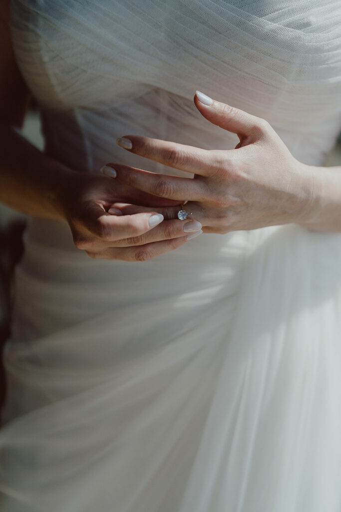 Person in a white dress adjusting a ring on their finger, with soft natural lighting.