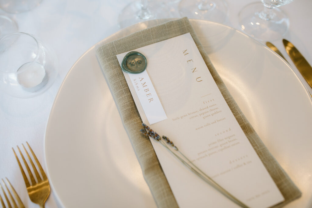 Golden cutlery and glasses around a white plate with a linen napkin, menu card, and dried lavender sprig.