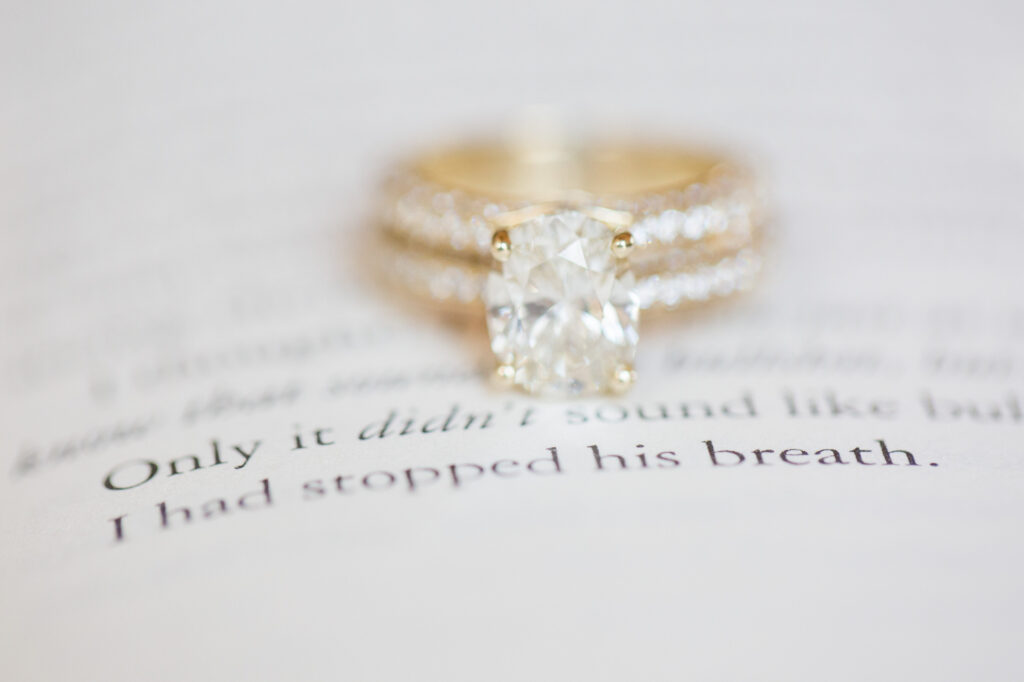 A gold ring with a large square-cut diamond is placed on an open book, with text slightly blurred in the background.