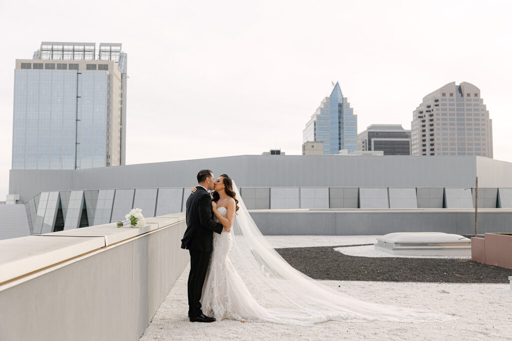 A couple in wedding attire embraces on a rooftop, with modern city buildings in the background—a perfect moment orchestrated by their Sacramento wedding planner.