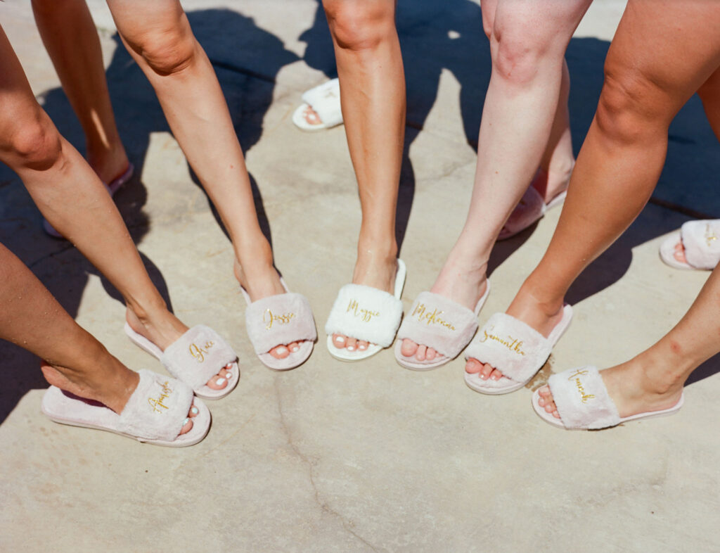 Seven people in fluffy slippers with names in gold script stand together on a stone surface.