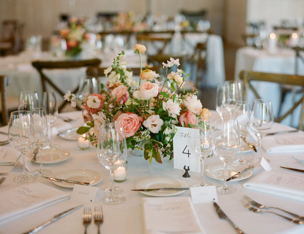 Elegant table setting with a floral centerpiece featuring pink and white flowers. Wine glasses, plates, and silverware are arranged neatly around a table number card reading "4.