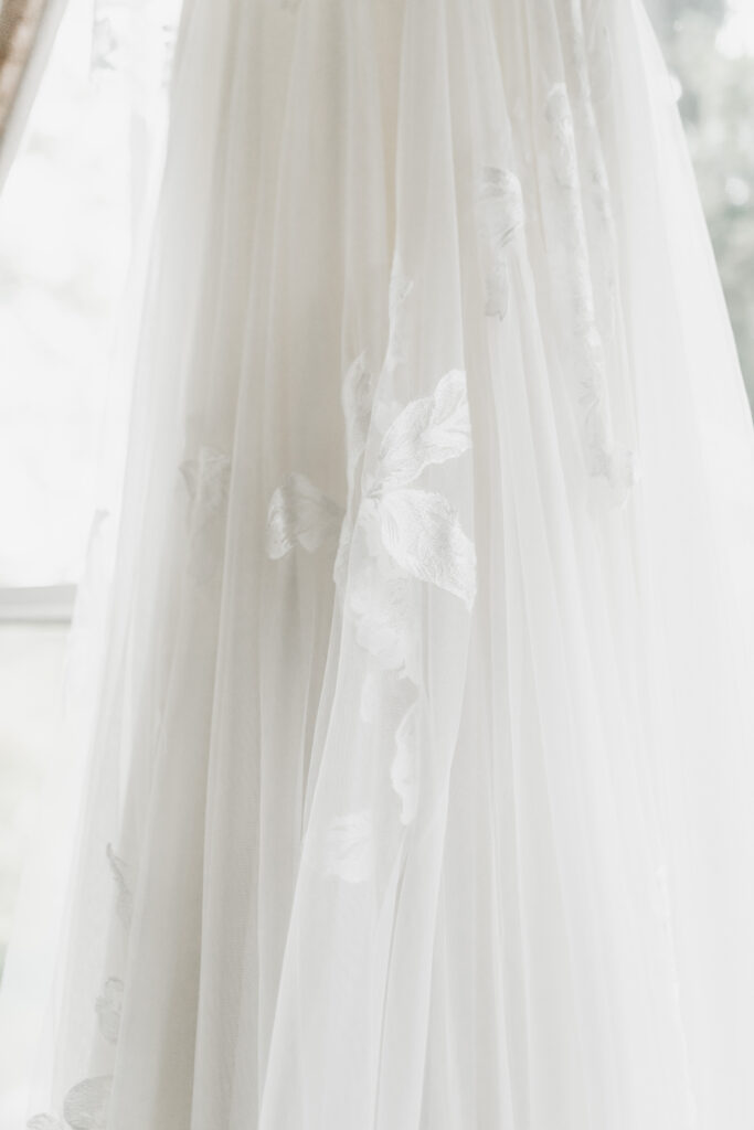 Close-up of a flowing white wedding dress with delicate embroidered floral patterns.