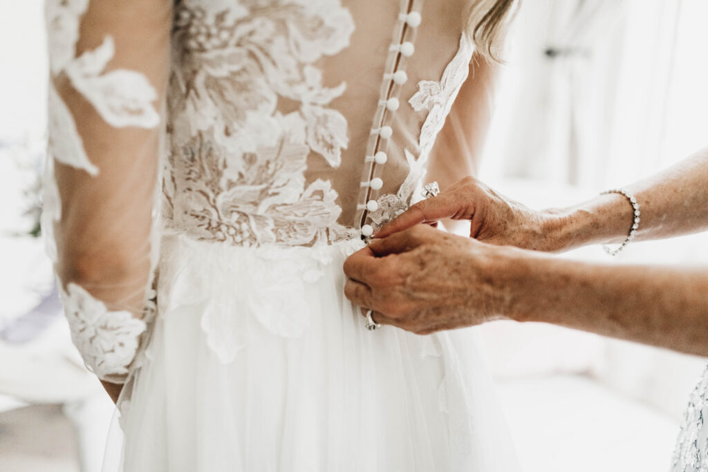Person fastening the buttons on a lace wedding dress.