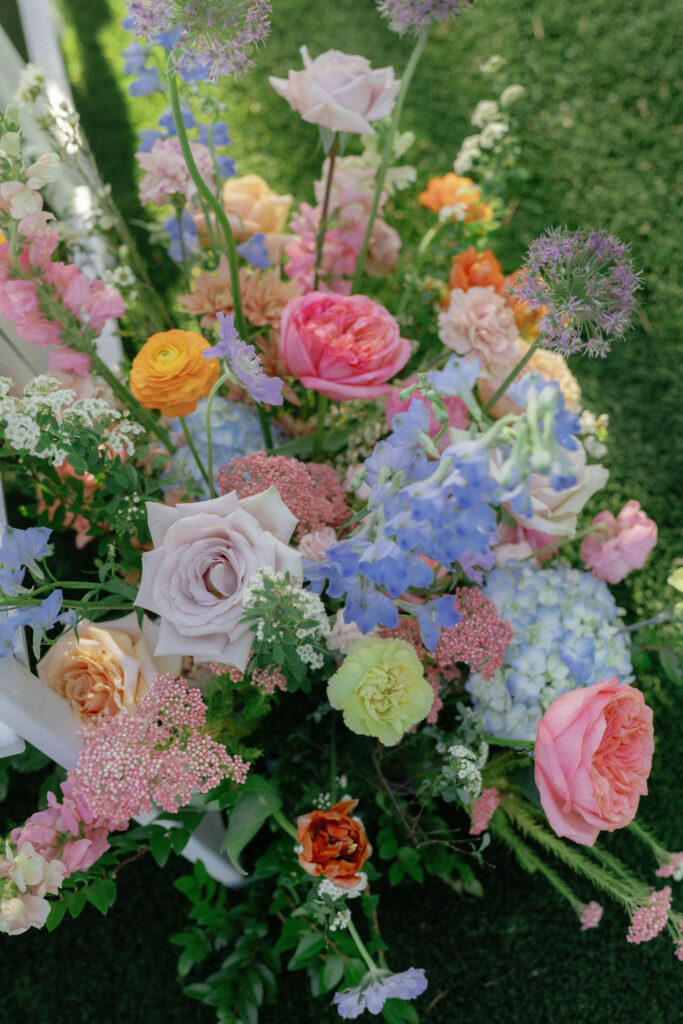 A colorful floral arrangement featuring roses, hydrangeas, and a variety of other flowers set against a green grass background.