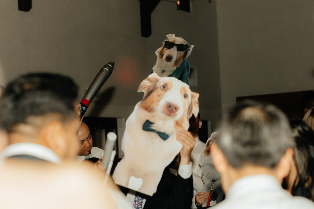 People at an event holding oversized cutouts of dogs, one wearing sunglasses and the other with a bow tie.