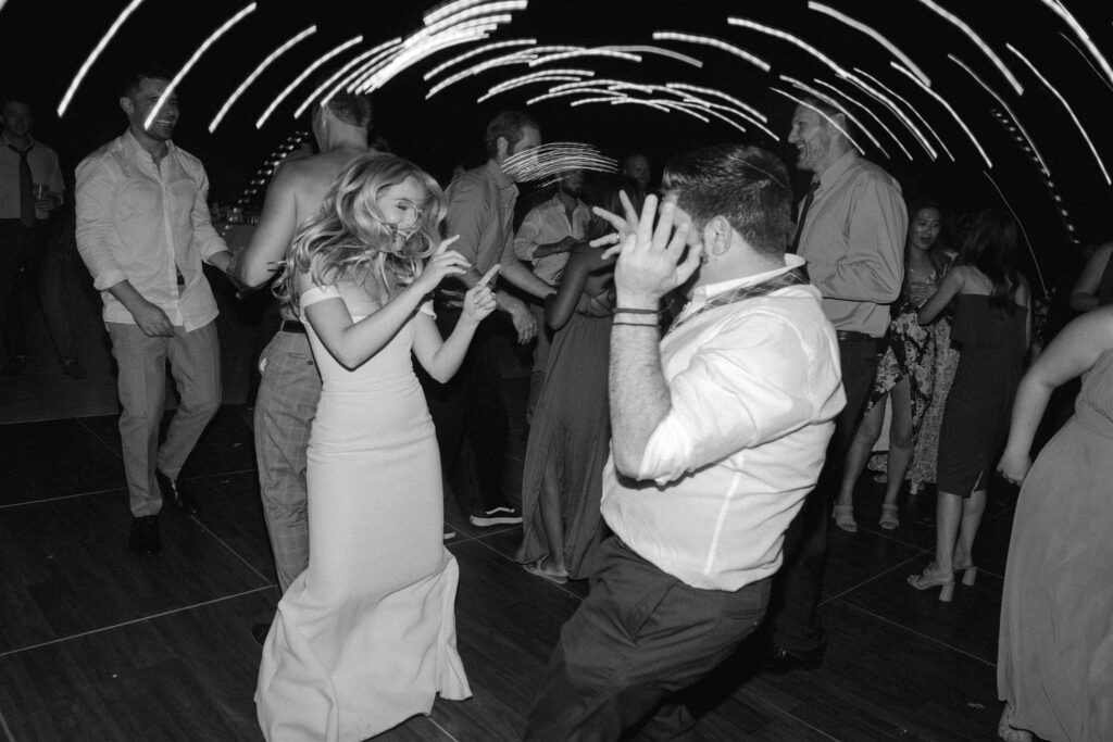 People are dancing energetically at a party with light trails above them, creating a dynamic atmosphere.