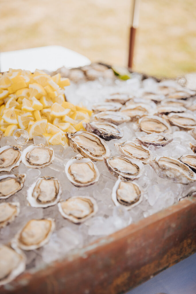 Fresh oysters on the half shell arranged on a bed of ice with a pile of lemon wedges nearby.